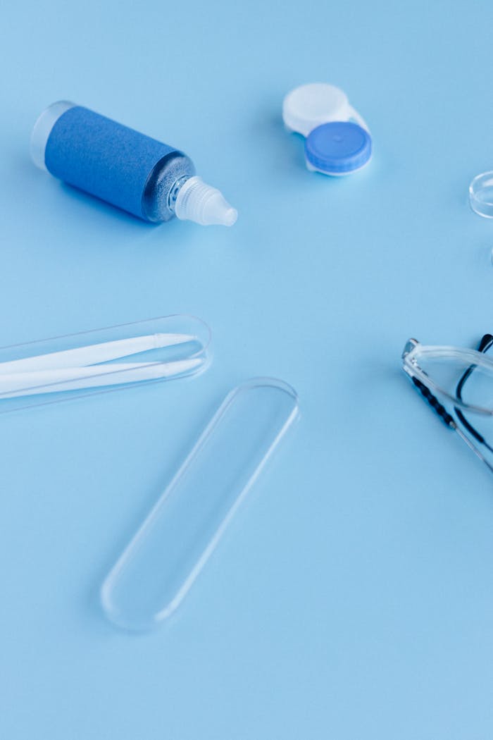 Flat lay of contact lens solution, cases, and tweezers on a blue surface.
